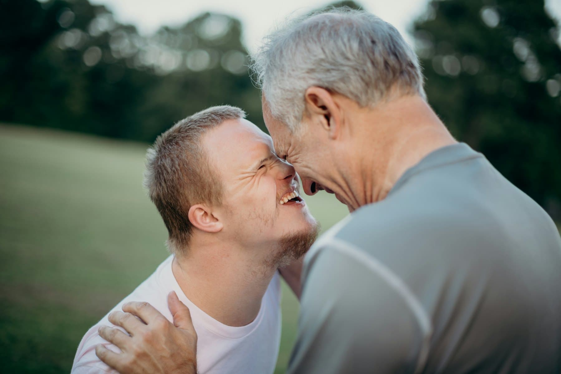 A young man with Down syndrome sharing a joyful moment with an older man outdoors